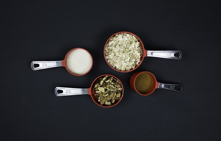 Red Measuring Cups With Oats, Nuts, And Spices On Black Background