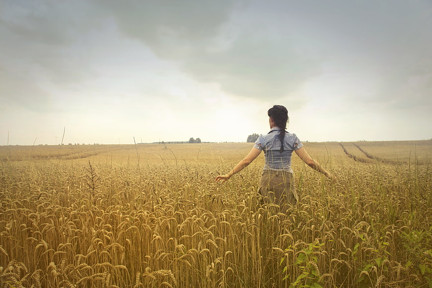 Woman standing in golden wheat field with arms outstretched