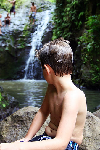 Young Boy Sitting by Waterfall in Nature