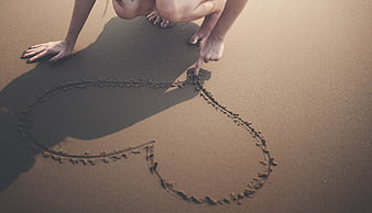 Woman Drawing Heart in Sand on Beach