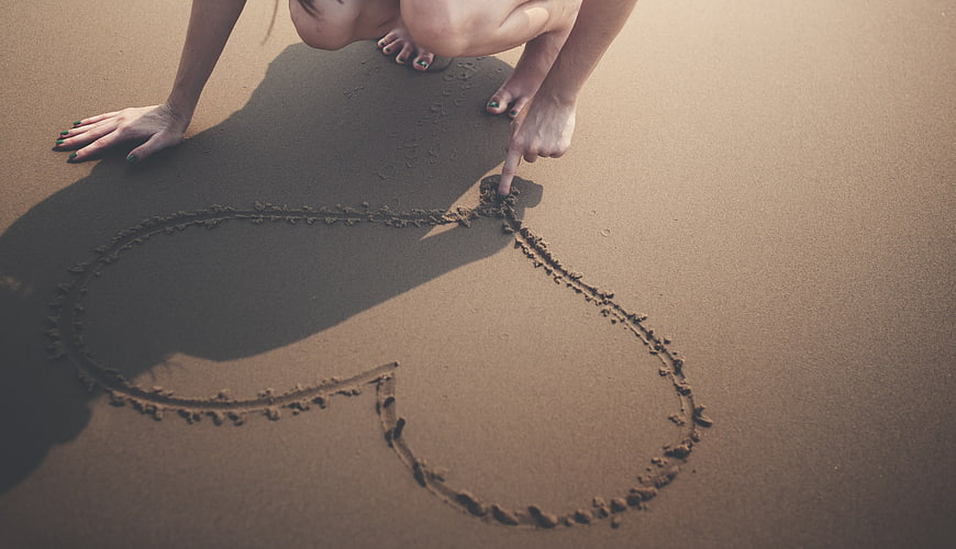 Woman Drawing Heart in Sand on Beach