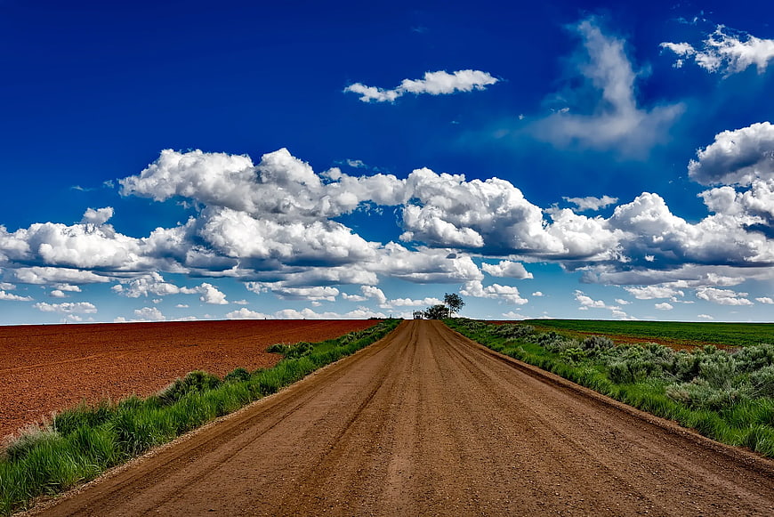 Dirt Road Through Red Soil Fields Under Blue Sky