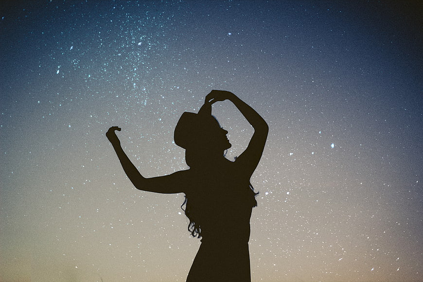 Silhouette of woman dancing under starry night sky