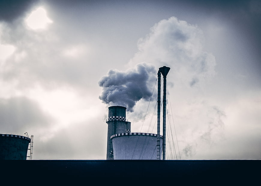 Industrial cooling towers emitting smoke against cloudy sky