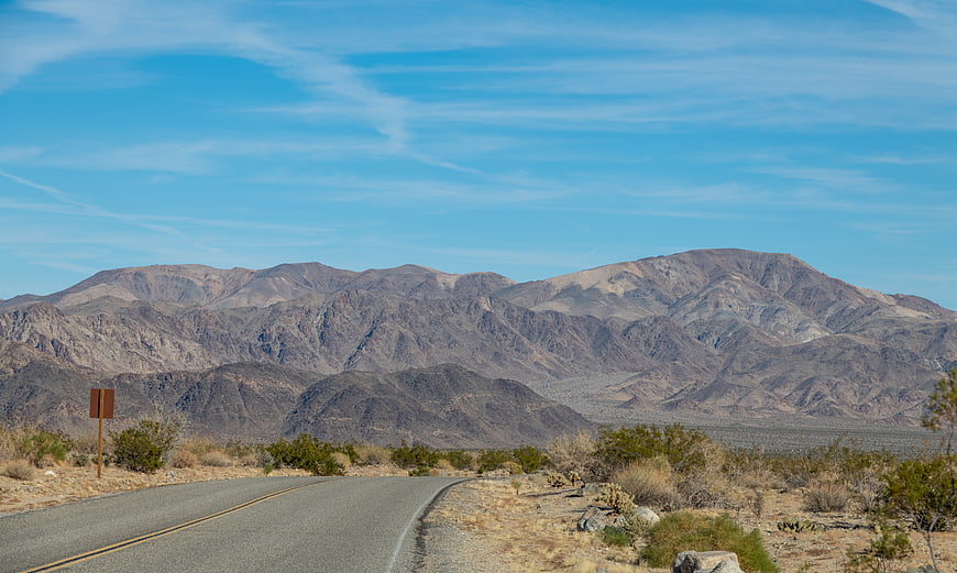 Empty desert highway winding through arid mountains under blue sky