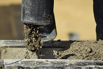 Close-up of wet concrete being poured from a black hose into a construction form