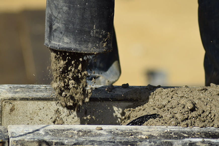 Close-up of wet concrete being poured from a black hose into a construction form