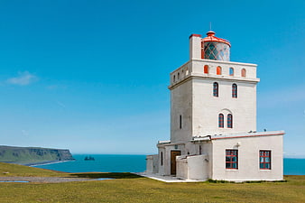 White Lighthouse on Green Cliff Overlooking Blue Ocean