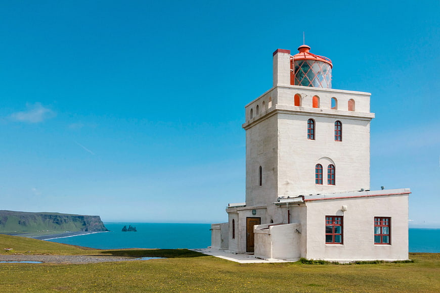White Lighthouse on Green Cliff Overlooking Blue Ocean