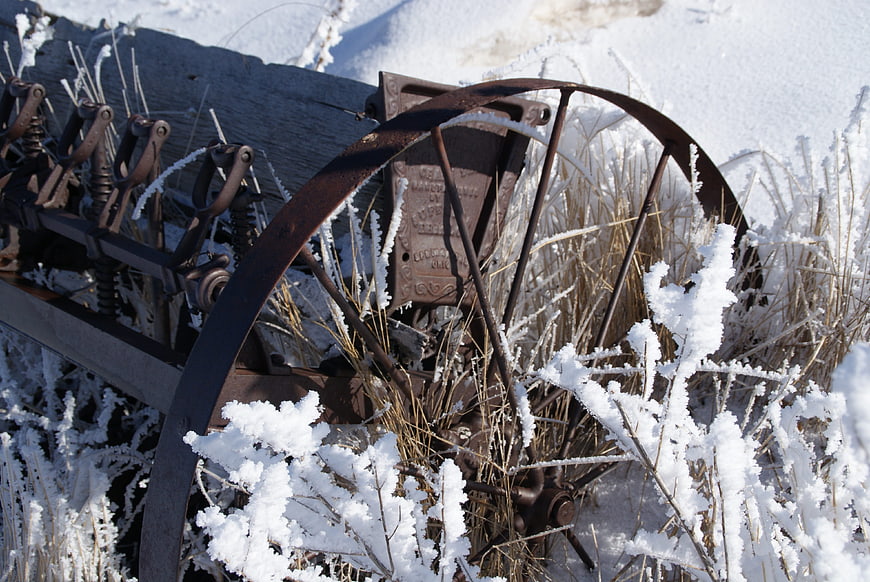 Rusty antique farm planter wheel covered in winter frost