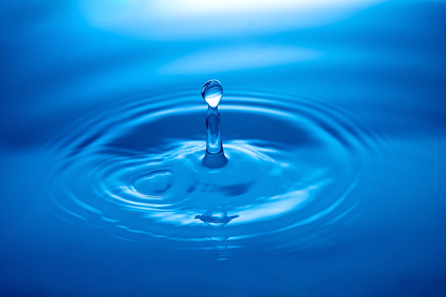 Blue water droplet splash with ripples on calm surface