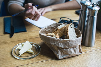 Bread basket and butter on wooden table with person writing