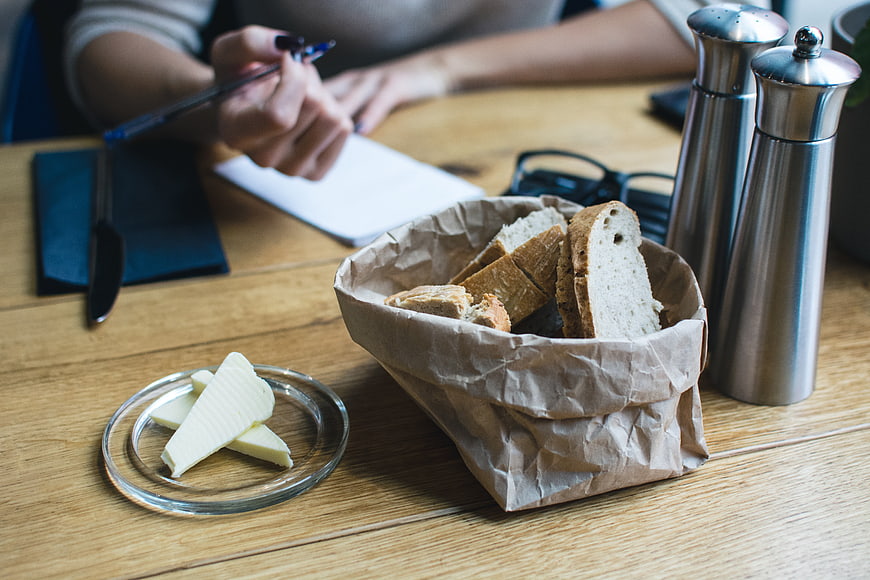 Bread basket and butter on wooden table with person writing