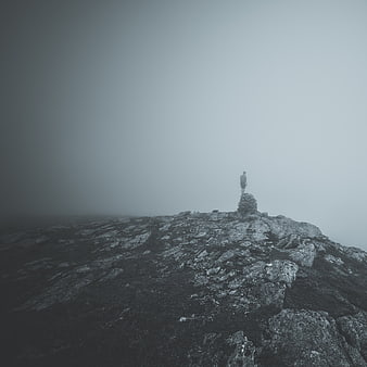 Lone hiker standing on misty mountain peak in fog