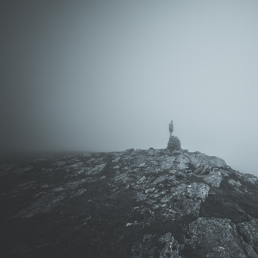 Lone hiker standing on misty mountain peak in fog