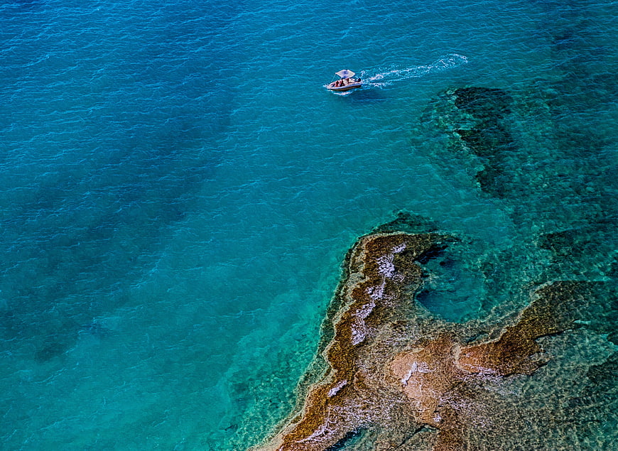Aerial View of Boat in Turquoise Ocean Near Rocky Coast