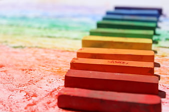 Colorful chalk sticks arranged in rainbow gradient on textured background