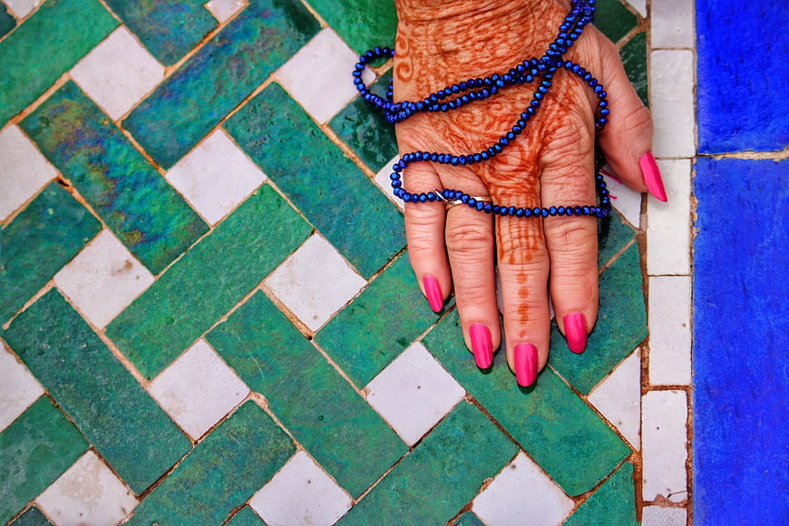 Henna decorated hand with blue beads on green mosaic tile