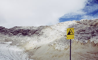 Yellow Falling Rocks Warning Sign Against Snowy Mountain