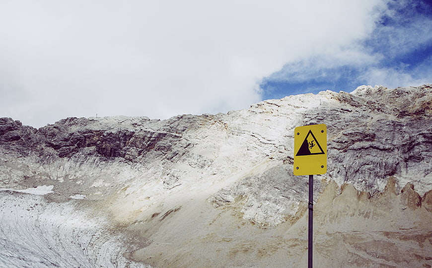 Yellow Falling Rocks Warning Sign Against Snowy Mountain
