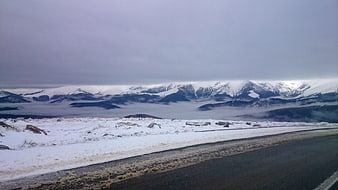 Snowy mountain road with foggy valley and overcast sky