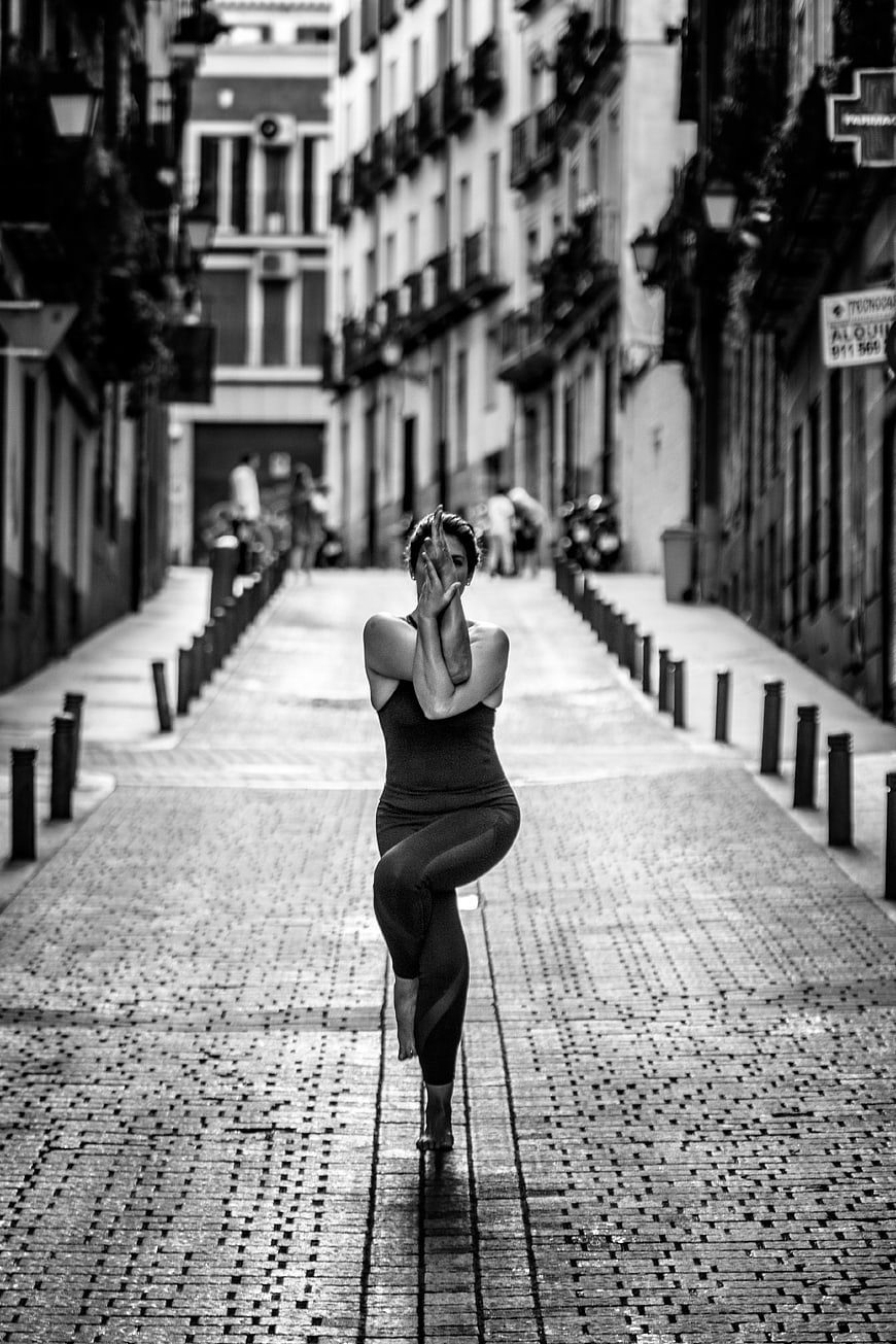 Woman performing yoga tree pose on a cobblestone street in Madrid