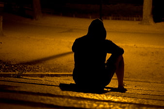Silhouette of Lonely Hooded Man Sitting on Sidewalk at Night