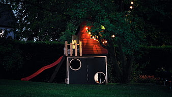 Wooden playhouse with slide and string lights at night