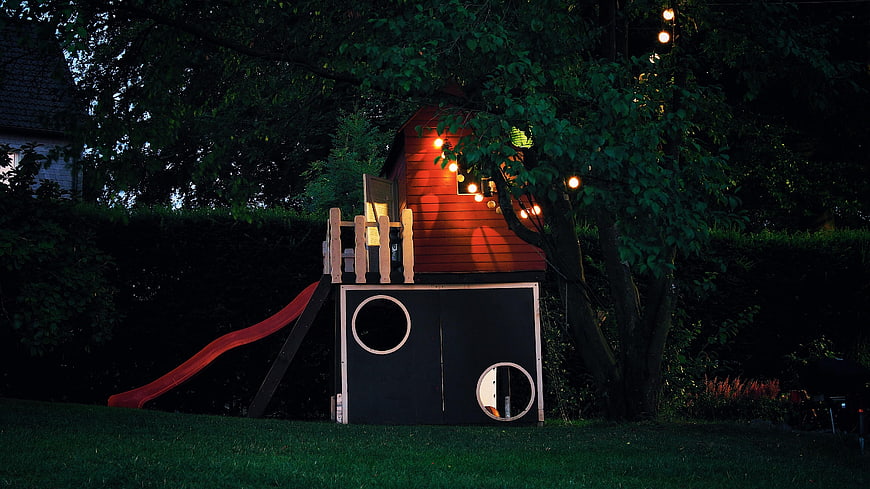 Wooden playhouse with slide and string lights at night