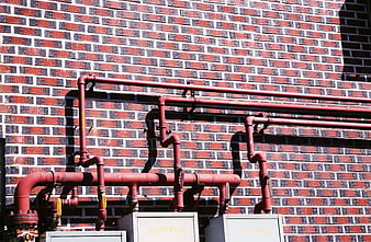 Red Industrial Pipes Against Patterned Brick Wall