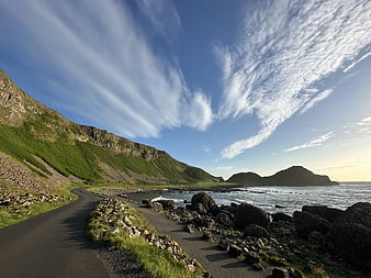 Coastal Road Along Rocky Shoreline With Green Hills And Blue Sky