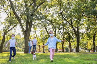 Family with dog running in park wearing face masks