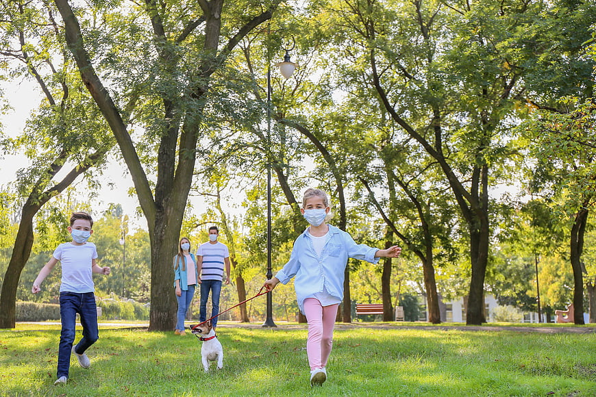 Family with dog running in park wearing face masks
