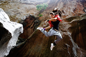 Woman in dynamic fighting stance leaping over rocky canyon