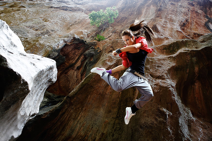 Woman in dynamic fighting stance leaping over rocky canyon