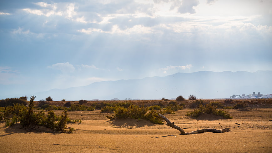 Sunbeams over dry desert landscape with distant mountains