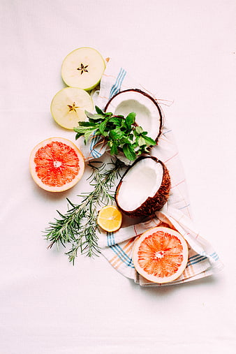 Flat lay of fresh coconut, grapefruit, apple, and herbs on white