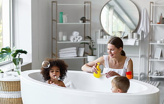 Happy mother and two children playing with bubbles in bathtub