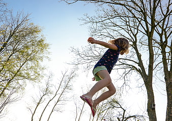 Young girl jumping in the air against blue sky and trees