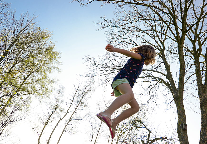 Young girl jumping in the air against blue sky and trees