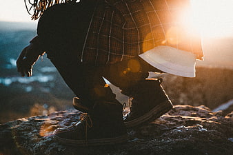 Man Squatting on Rocky Cliff at Sunset