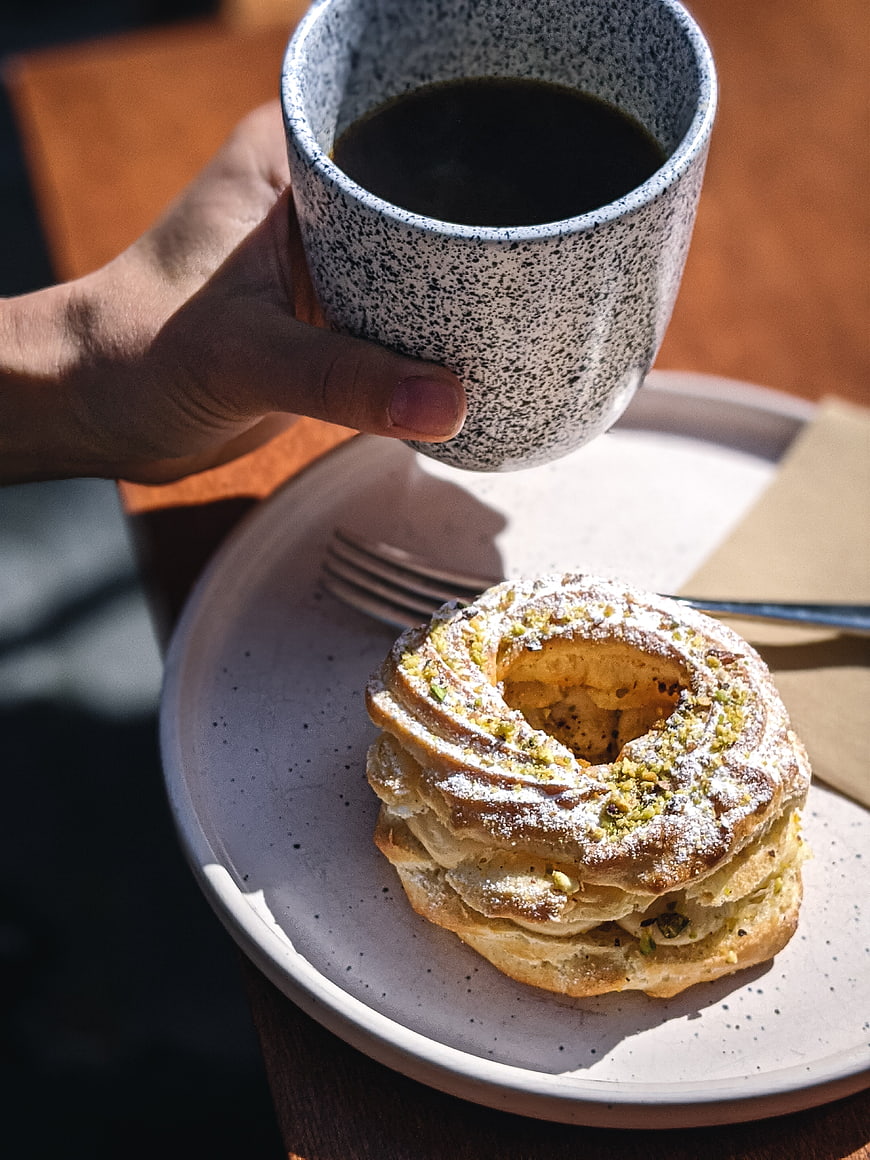 Hand holding coffee cup with pistachio pastry on plate