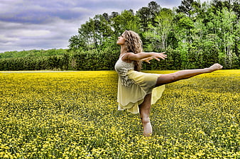 Woman performing dance pose in blooming yellow wildflower field