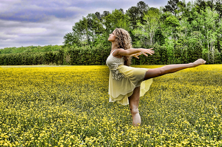 Woman performing dance pose in blooming yellow wildflower field