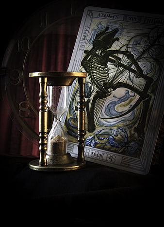 Vintage brass hourglass and tarot death card on dark background