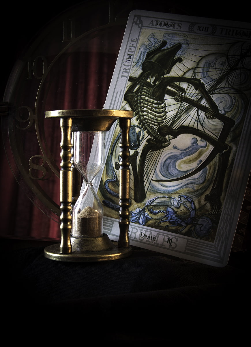 Vintage brass hourglass and tarot death card on dark background