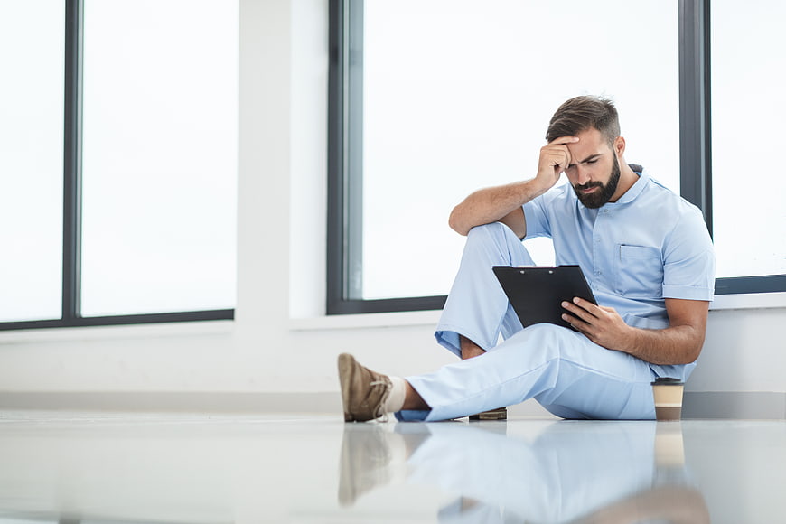 Stressed male nurse sitting on hospital floor reading clipboard