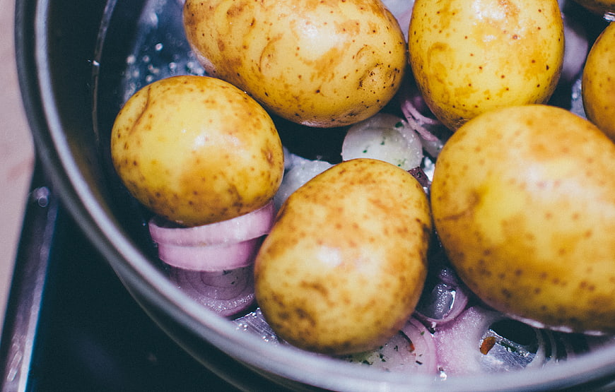 Close-up of raw potatoes and red onions in a cooking pot