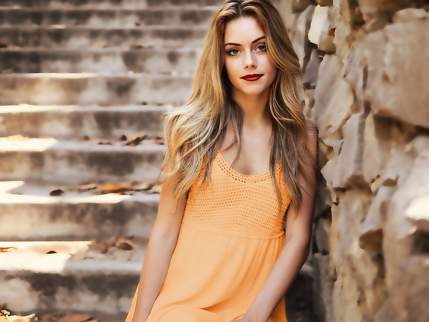 Woman in Orange Dress Leaning Against Stone Wall