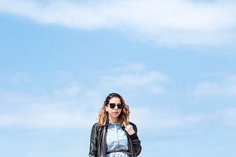 Woman in leather jacket and sunglasses against blue sky